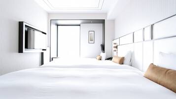 A modern hotel room with a large bed, a flat-screen TV mounted on the wall, and a bedside table with a lamp.