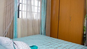 Een slaapkamer met een bed, gordijnen, een houten kledingkast en een raam met uitzicht.