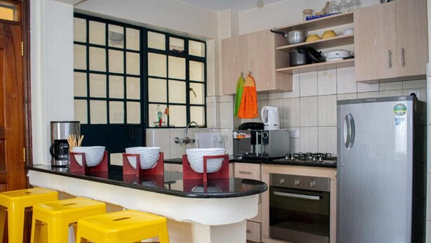 Een keuken met een centraal eiland, gele krukken, een koelkast, een fornuis en diverse keukenapparaten.