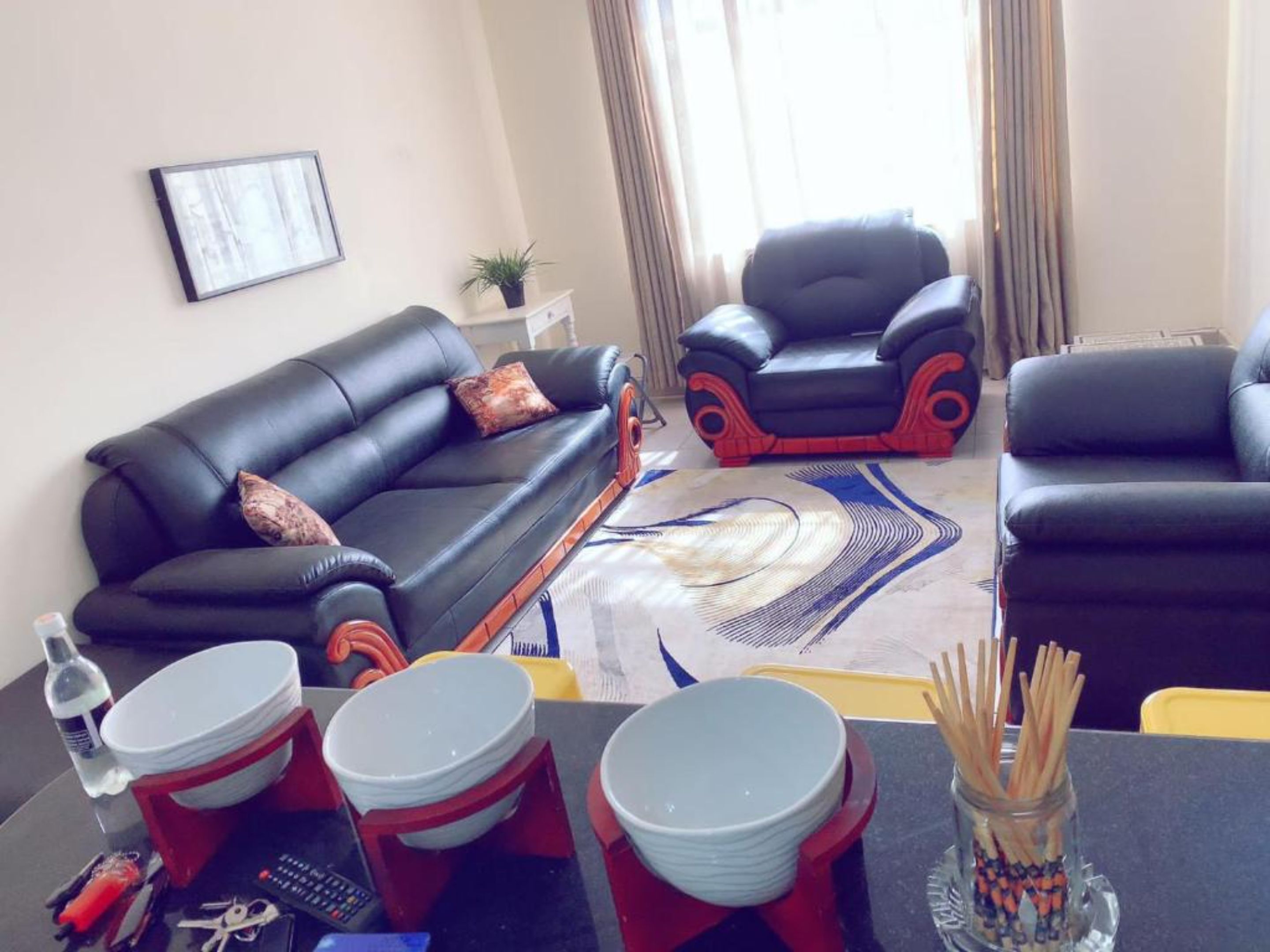 A living room with a black leather sofa, a matching armchair, and a dining table with stacked plates and cutlery.