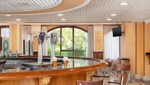 Zona de bar con un mostrador de madera curvo, taburetes y un ventanal con cortinas.