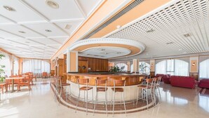 Un vestíbulo amplio con una zona de bar central, diferentes disposiciones de asientos y un diseño de techo moderno.
