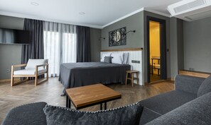 A modern hotel room with a bed, a wooden table, a sofa, and a TV mounted on the wall. - Istanbul Old City Colorful Houses Balat PETRION Hotel (Istanbul)