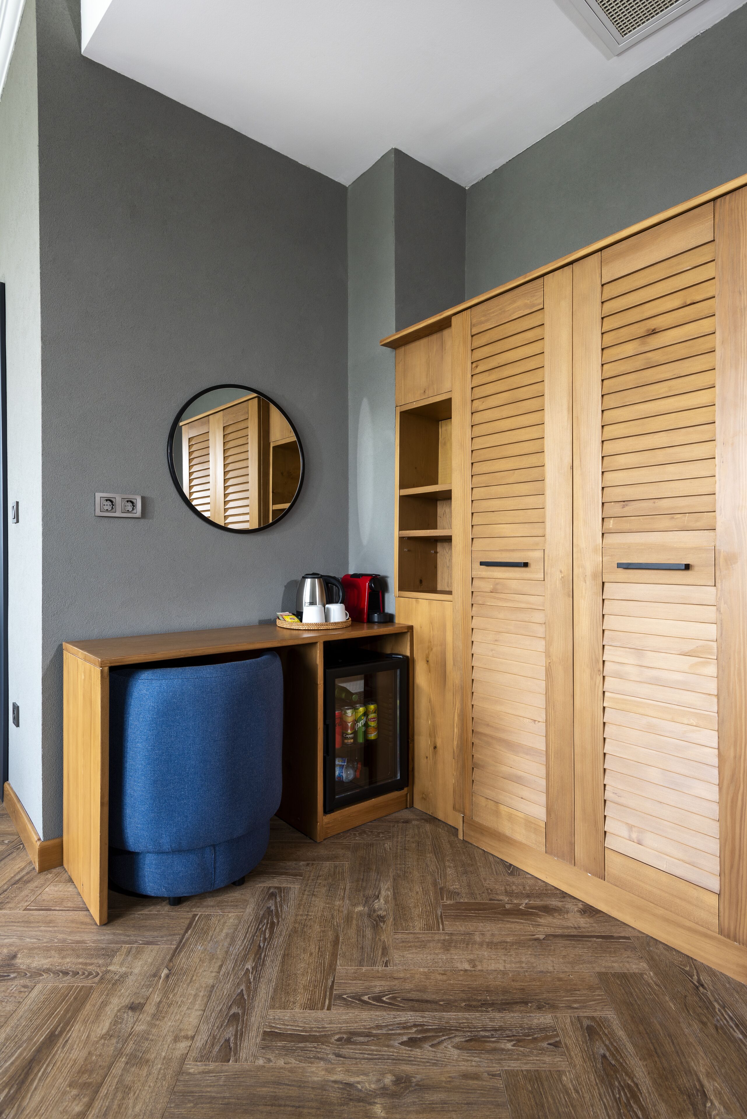 A room with a wooden desk, a blue chair, a mirror, and a wardrobe.