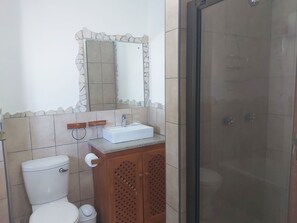A bathroom with a toilet, sink, mirror, and shower.