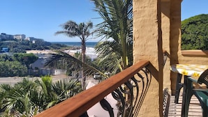 A balcony with a view of the beach and ocean, surrounded by palm trees and a building. - Crayfish Inn No.8 (Margate)