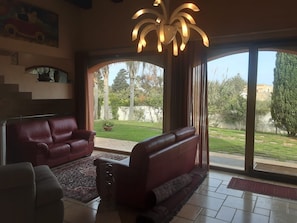 A living room with a red sofa, a coffee table, and a large window with a view of a garden. - Villa Dammusello with Pool, Garden & Wi-Fi (Marsala)