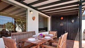 An outdoor dining area with wooden furniture, a glass wall, and a dark wooden door. - Holiday Home "Villa Mar" close to the Beach with Sea View, Pool & Wi-Fi (Teguise)