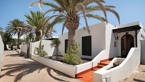 A modern building with a white exterior, a red-tiled entrance, and palm trees. - Holiday Home "Villa Mar" close to the Beach with Sea View, Pool & Wi-Fi (Teguise)