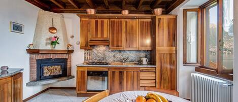 A kitchen with wooden cabinets, a stone fireplace, and a dining table with a fruit basket.