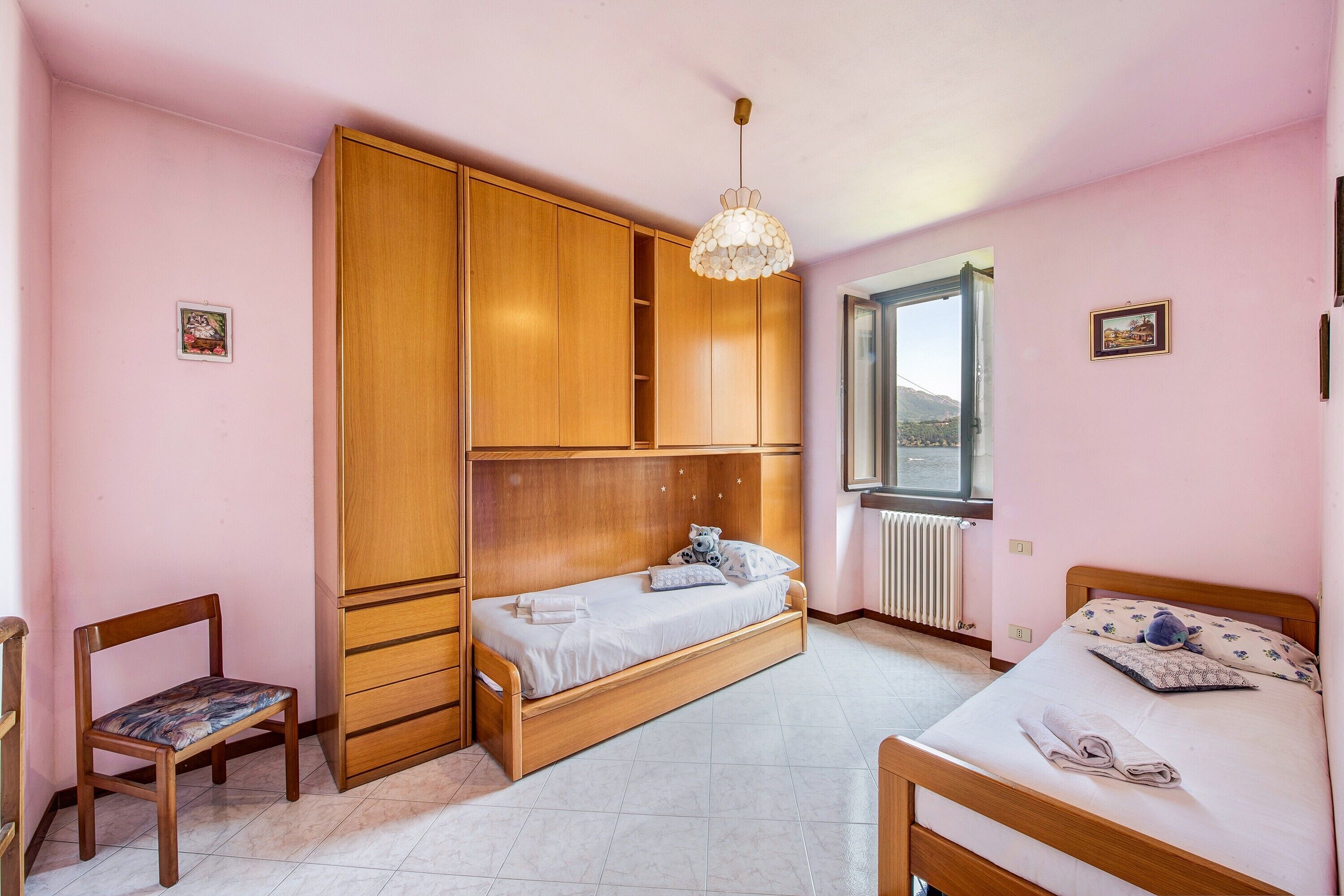 A bedroom with a bunk bed, a single bed, a wooden wardrobe, a chair, and a window with a view.