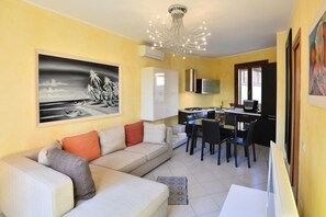 A living room with a sofa, a dining area with chairs, a kitchen with a stove, and a painting on the wall.