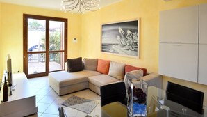 A living room with a sofa, a dining table, a chandelier, a painting, and a view through a glass door. - Holiday Apartment 'Luxury Guesthouse Pula' with Garden, 2 Terraces & Wi-Fi (Pula)