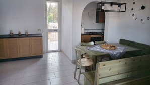 A kitchen with a dining area, wooden cabinets, a tiled floor, and a wall clock. - Pet-Friendly 'Villa Andrea' with Sea View, Garden & Wi-Fi (Manduria)
