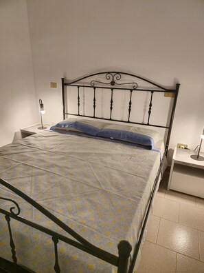 A bed with a metal frame, a bedside table with a lamp, and a wall socket.
