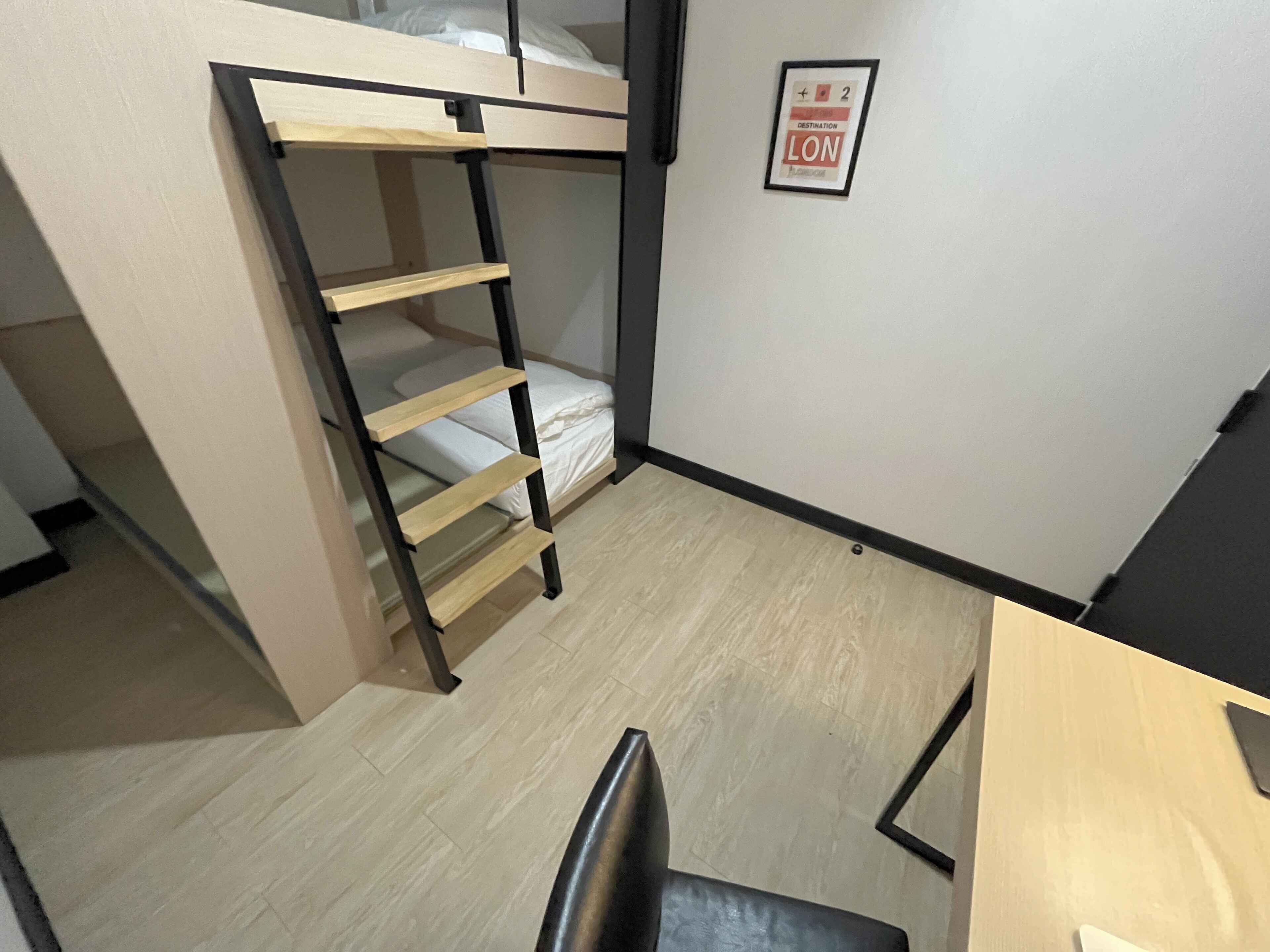 Un lit superposé avec une échelle en bois, un petit bureau et un panneau encadré accroché au mur.