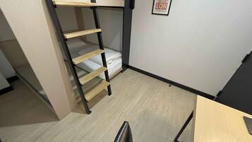 Un lit superposé avec une échelle en bois, un petit bureau et un panneau encadré accroché au mur.