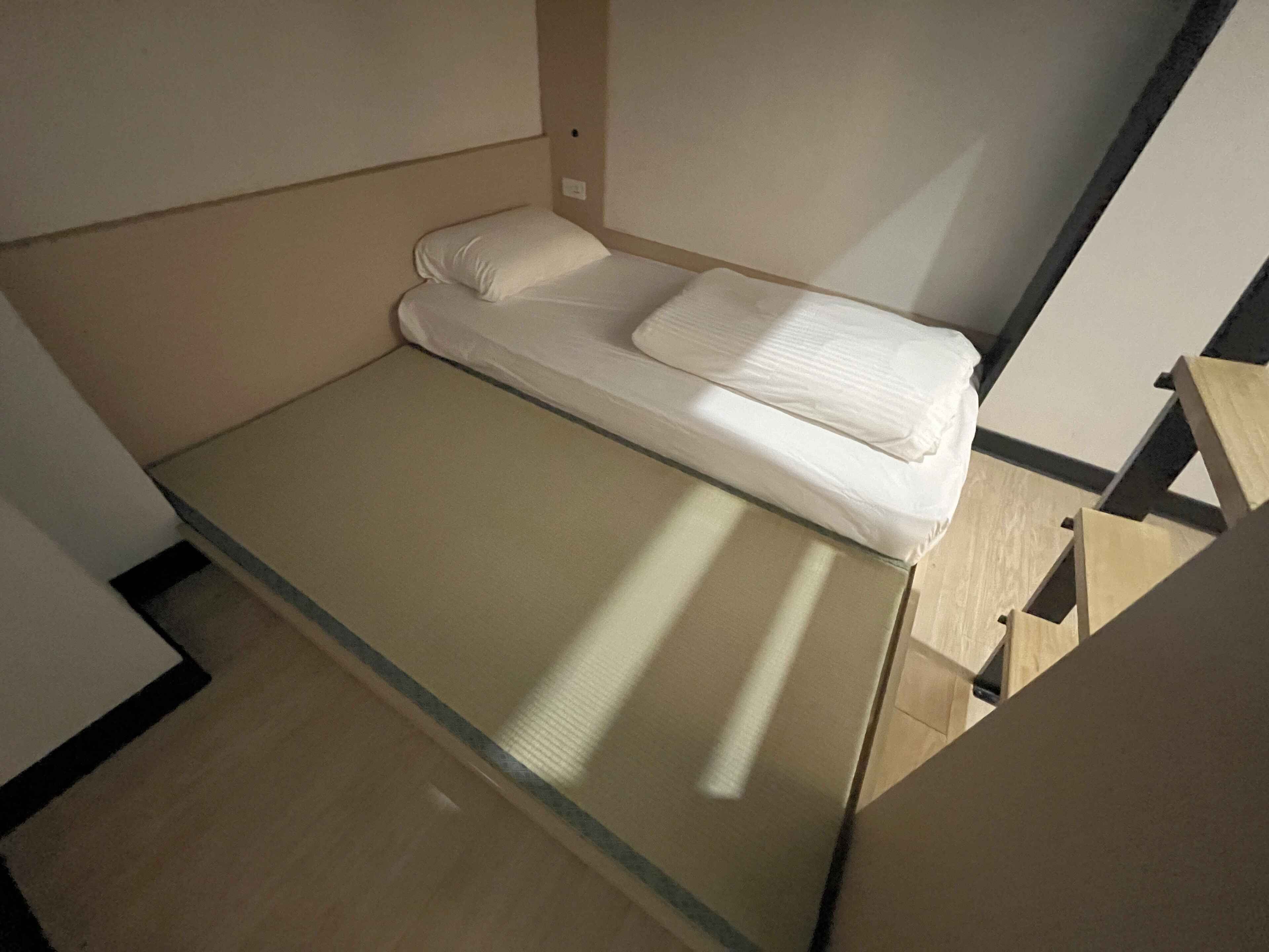 A small, single-bed room with a simple, clean design, featuring a mattress and pillows.