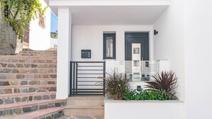 A white building with stone steps leading to a gated entrance, a small planter with plants, and a door with a dark frame. - Spacious apartment in Cómpeta with shared pool and jacuzzi (Cómpeta)