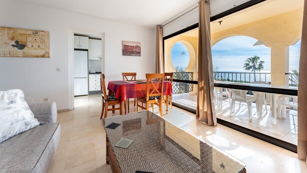 A modern living room with a glass table, a sofa, and a balcony with outdoor seating. - Apartment 'Sea Views Torre Oceano 7' with Shared Pool & Wi-Fi (Mijas costa)