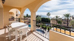A balcony with a table and chairs, a pool, and a view of the sea and neighboring buildings. - Apartment 'Sea Views Torre Oceano 7' with Shared Pool & Wi-Fi (Mijas costa)