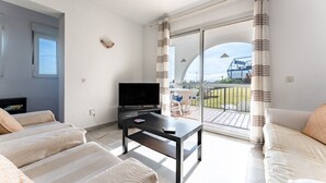 Et hotelværelse med fjernsyn, to stribede sofaer, et lille bord og en balkon med gardiner.