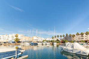 Un port de plaisance avec des bateaux amarrés, un ciel dégagé et des bâtiments bordés de palmiers en arrière-plan.