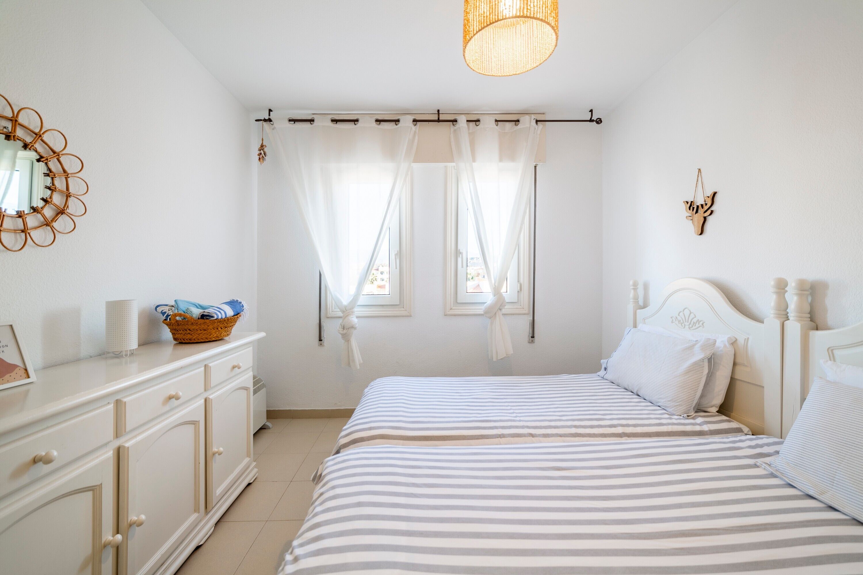 Une chambre à coucher avec un lit, des rideaux, une table de chevet, une lampe et un miroir fixé au mur.