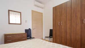 Ein Schlafzimmer mit einem Bett, einem Holzschrank, einem Schreibtisch mit Schubladen, zwei Stühlen und einer Wand-Klimaanlage.