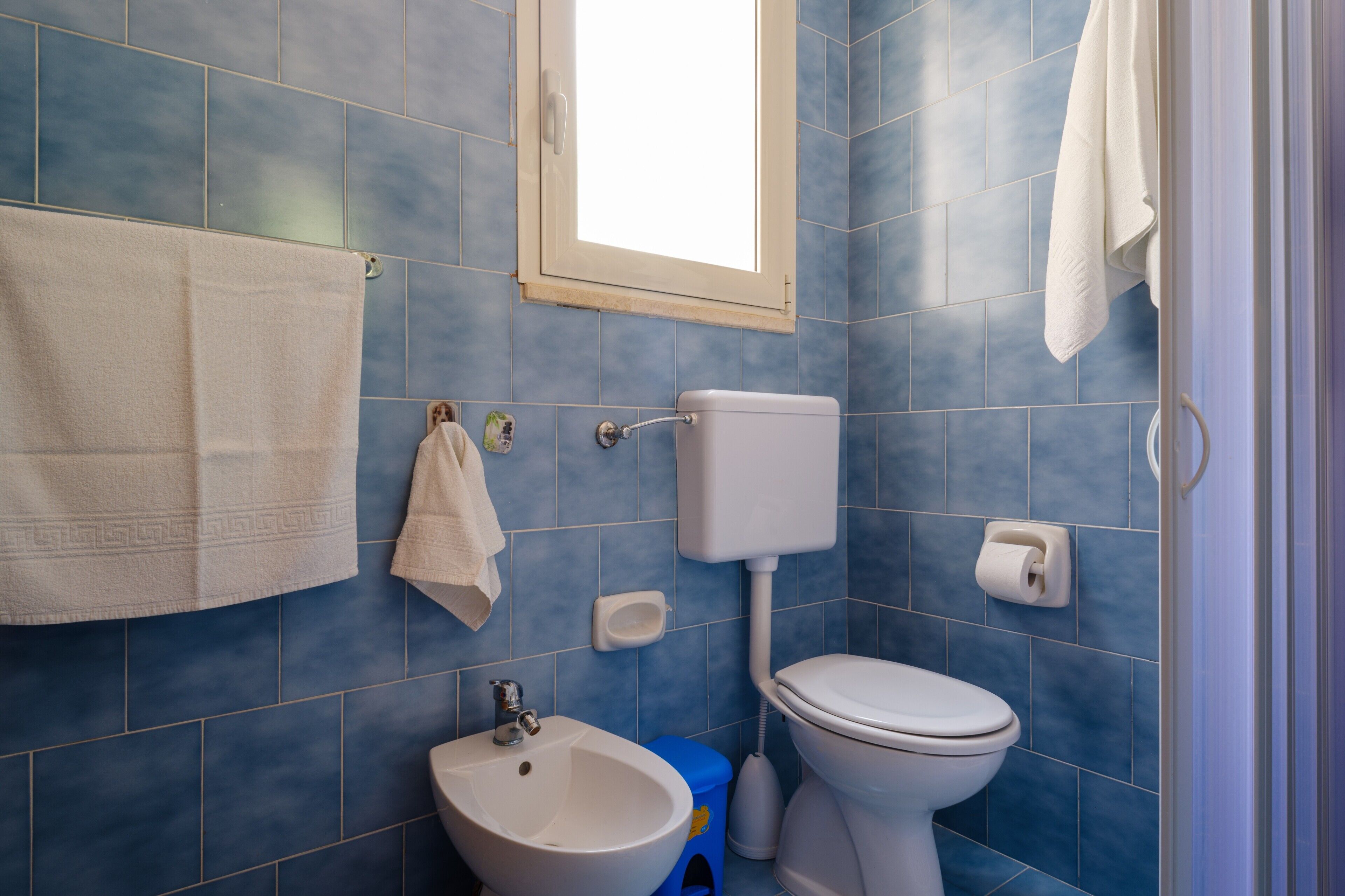 Ein Badezimmer mit blauen Fliesen, einer weißen Toilette, einem Waschbecken und einem Handtuch, das an der Wand hängt.