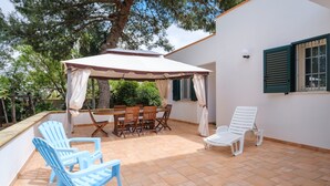 Un patio con mesa y sillas, una zona cubierta y una silla blanca.