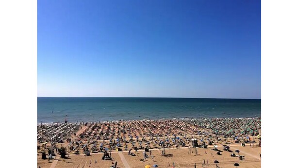 Una playa con numerosos sombrillas y tumbonas, lo que sugiere una gran cantidad de visitantes.