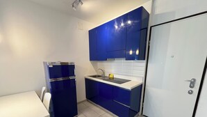 Una cocina compacta con armarios azules, una encimera blanca y un refrigerador pequeño.
