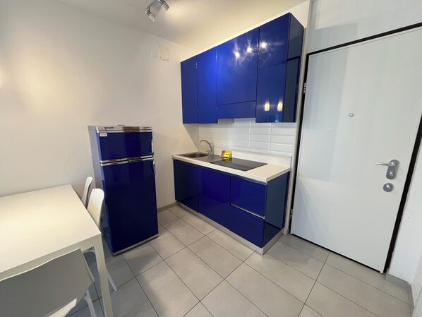 A compact kitchen with blue cabinets, a white countertop, and a small refrigerator.