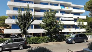 Un hotel de varios pisos con balcones, coches aparcados y zonas verdes.