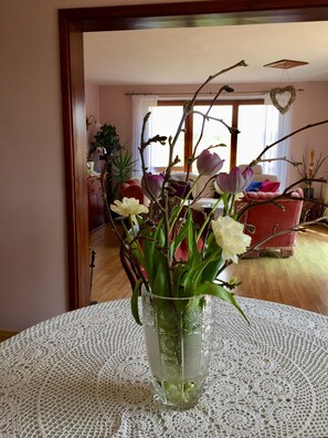 A room with a wooden floor, a lace tablecloth, a vase with flowers, and a red sofa.