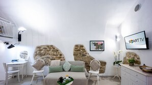 Una habitación moderna con una pared de piedra decorativa, una cama con colcha estampada verde y blanca, una mesita con una bandeja de objetos, un televisor en la pared y un armario blanco.