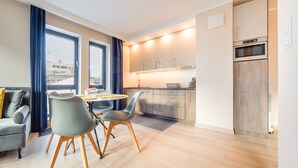 Una cocina moderna con armarios de madera, horno integrado y refrigerador. Hay una zona de comedor con mesa y sillas, y un sofá en la esquina.