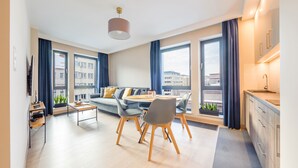 Un apartamento moderno con sala de estar, comedor y cocina. Cuenta con ventanas amplias, un sofá, una mesa de comedor con sillas y una encimera de cocina.
