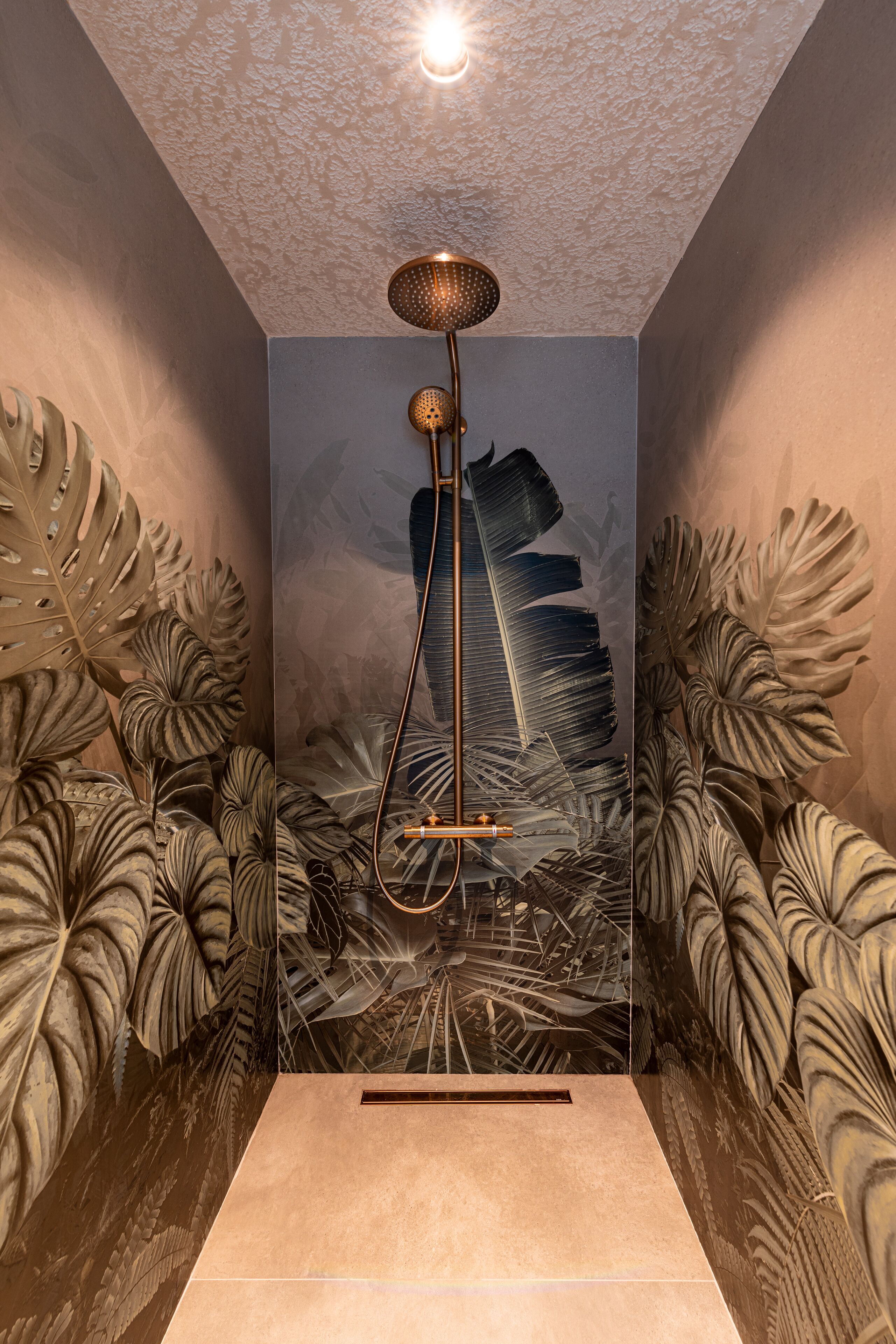 A bathroom with a shower, large decorative leaves on the walls, and a textured ceiling.