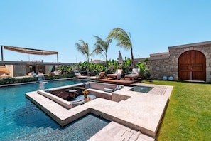 A luxurious pool area with lounge chairs, a seating area, and a stone wall.