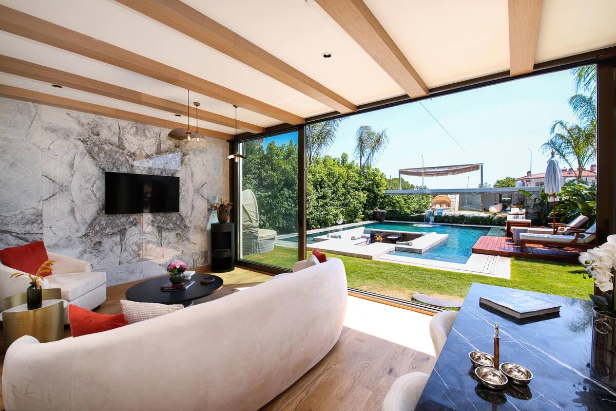 Un salon moderne doté d’un grand mur de verre, d’un téléviseur à écran plat, d’une piscine et de mobilier d’extérieur.