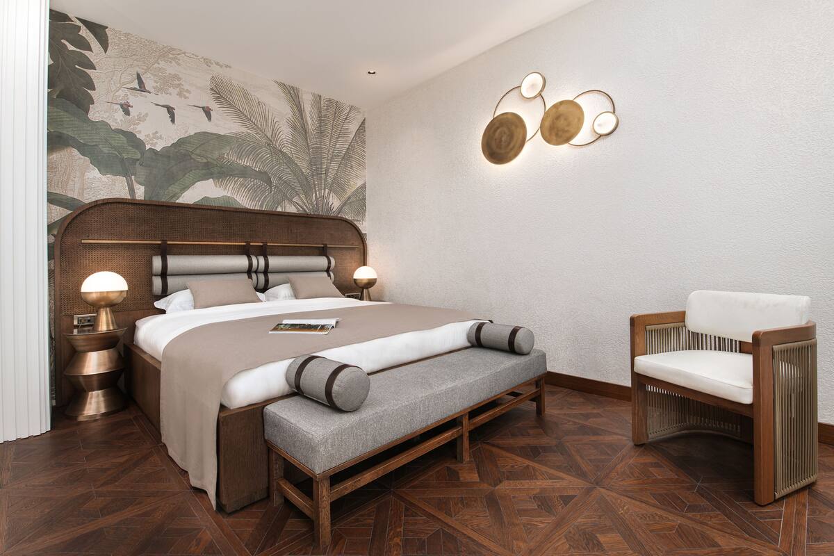 Une chambre avec un grand lit, une table de chevet avec une lampe, une chaise et une fresque murale.
