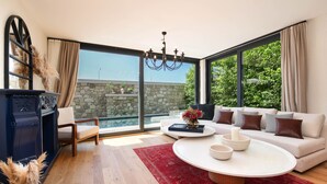 A modern living room with a large window, a stone wall, a chandelier, a sofa, and a coffee table. - Genesis Hotel (Cesme)