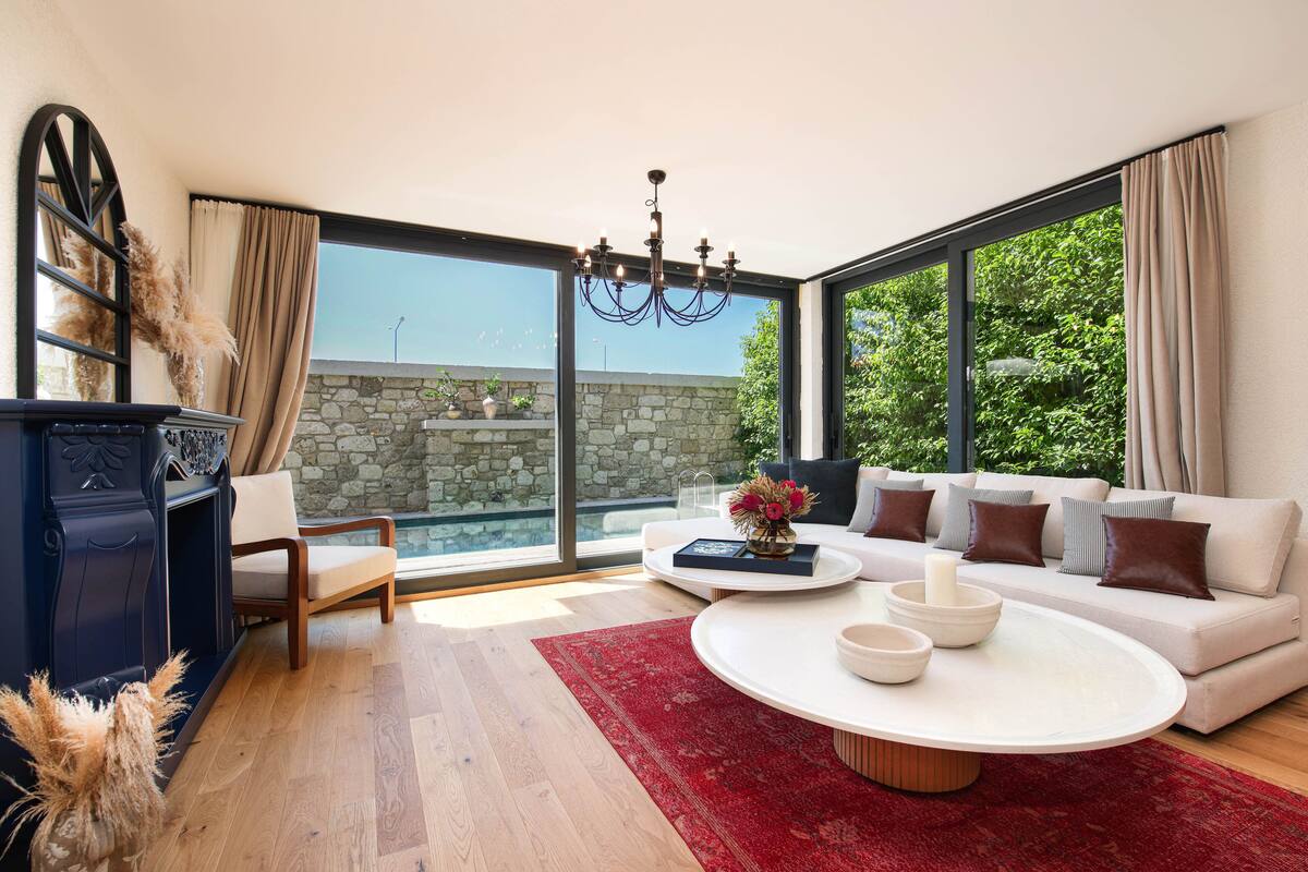 Un salon moderne avec une grande fenêtre, un mur en pierre, un lustre, un canapé et une table basse.