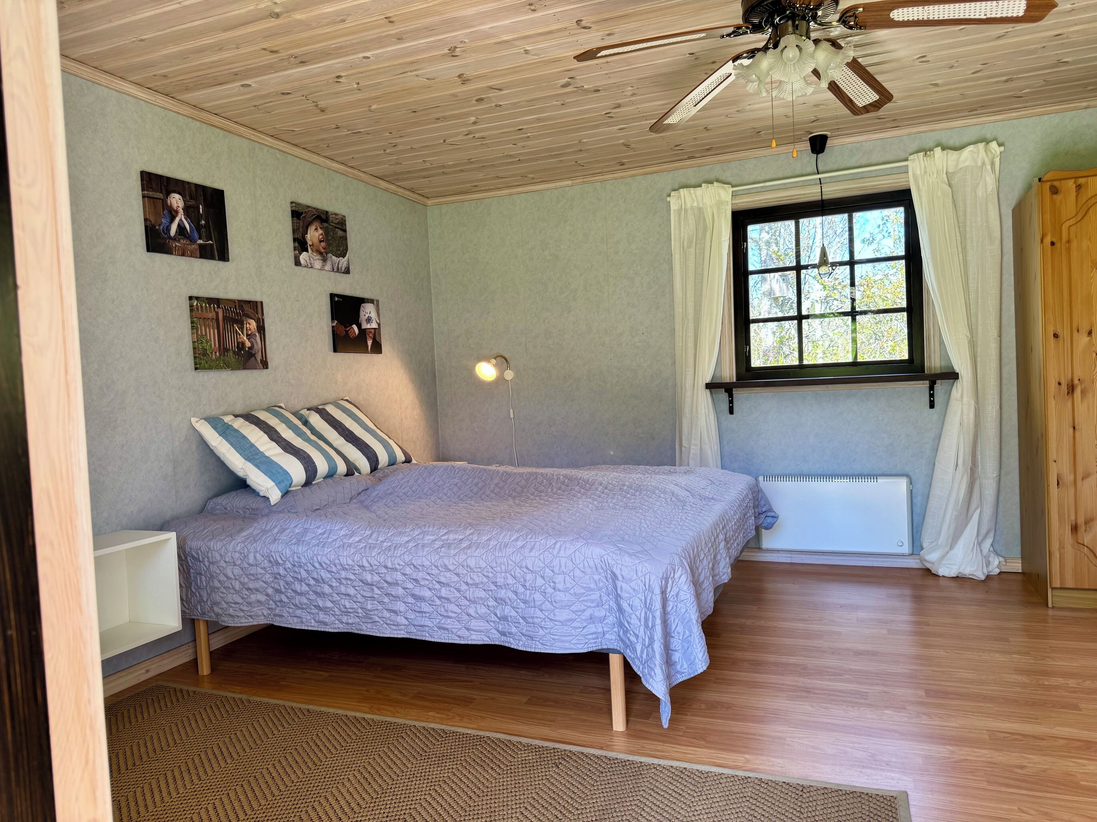 A bedroom with a bed, a ceiling fan, a window with curtains, and wall-mounted pictures.
