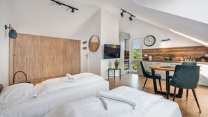 A modern bedroom with a large wardrobe, a bed with white linens, a small table with a plant, and a view of the kitchen through an open door. - Apartamenty Sun & Snow Baltic Sun (Sztutowo)