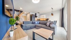 A modern living room with a sectional sofa, a wooden coffee table, and a staircase leading to an upper level. - Apartamenty Sun & Snow Baltic Sun (Sztutowo)