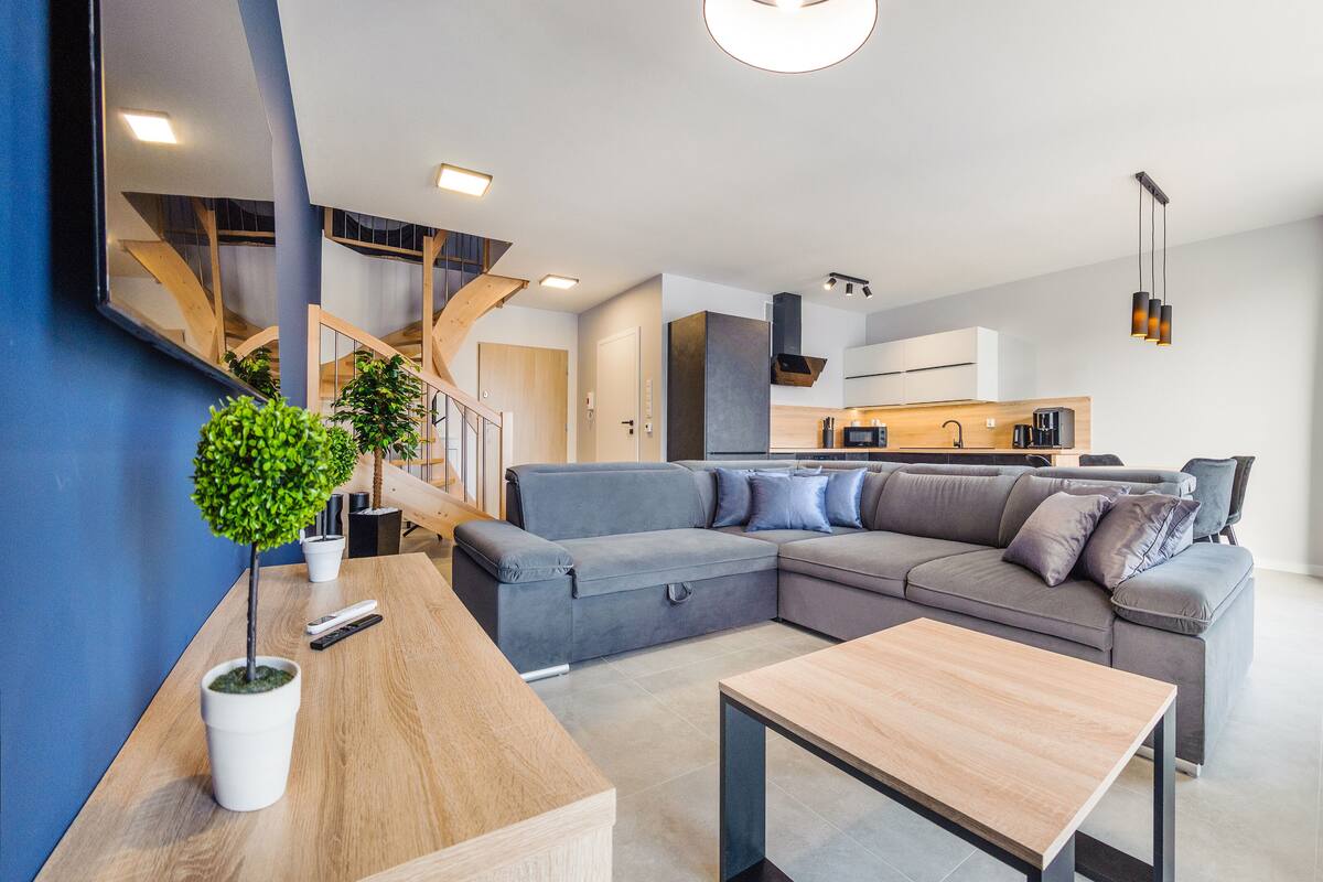 Ein modernes Wohnzimmer mit einer Eckcouch, einem Holztisch und einer Treppe zu einer oberen Ebene.