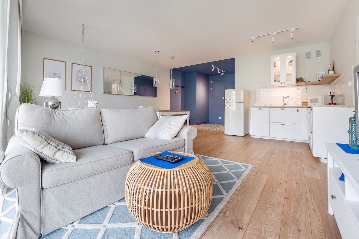 Ein modernes Wohnzimmer mit einem grauen Sofa, einem kleinen runden Holztisch und einem Fernseher auf einem weißen Schrank.